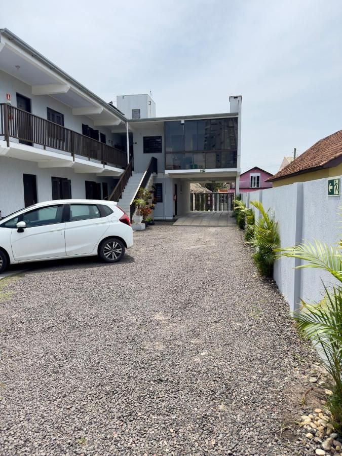 Estacionamento interno da pousada visto do portão, com o prédio de dois pisos ao fundo
