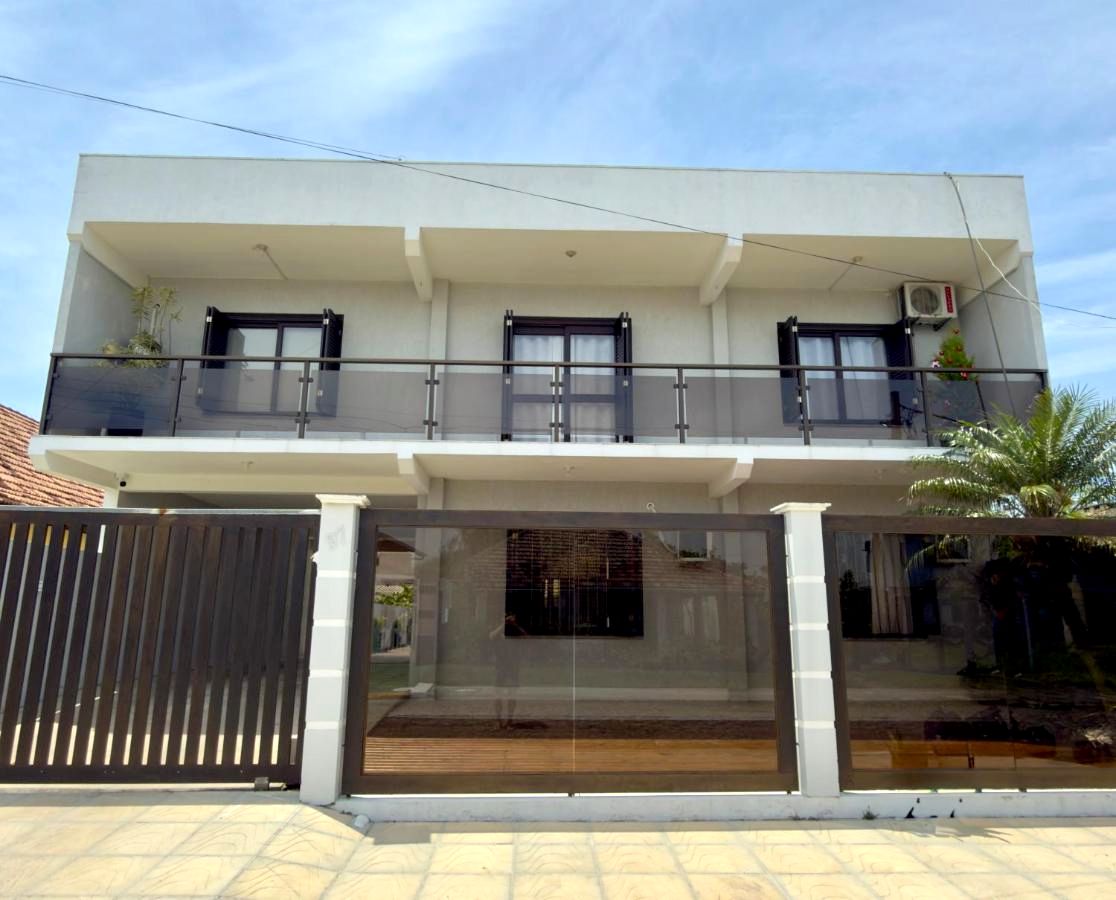 Fachada da Classe Pousada: prédio de dois pisos com sacada, portão escuro e palmeira, no Centro de Imbé