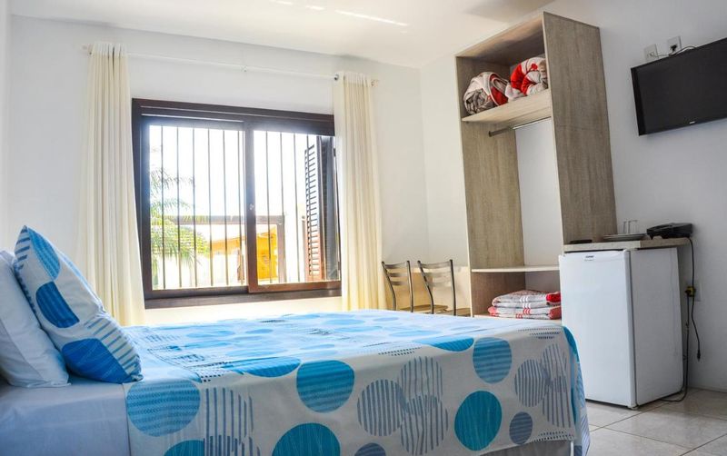 Quarto de casal com cama de estampa azul, janela, frigobar e TV