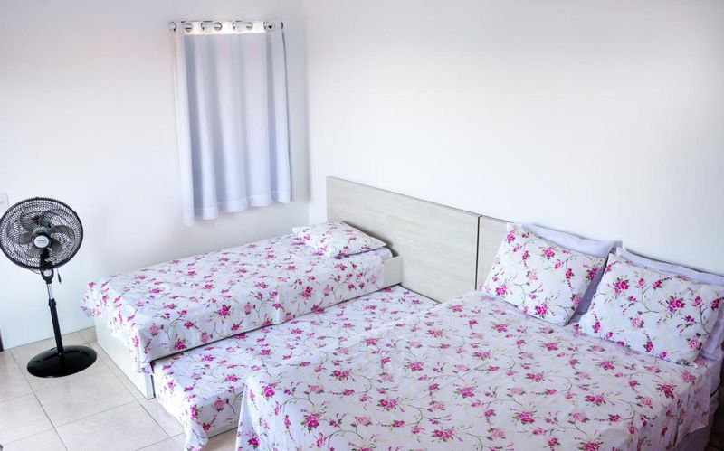 Quarto com duas camas de roupa floral e ventilador