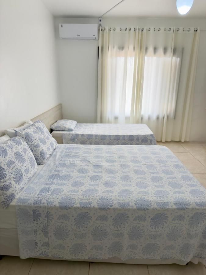 Quarto com cama de casal e cama de solteiro, ar-condicionado e cortinas claras