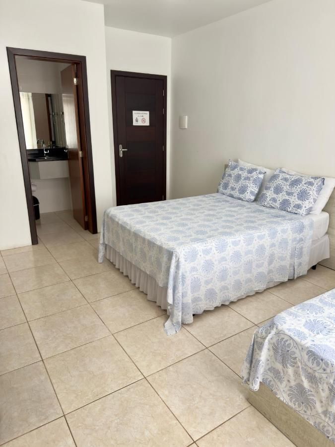 Quarto com cama de casal e uma terceira cama, porta do banheiro ao fundo